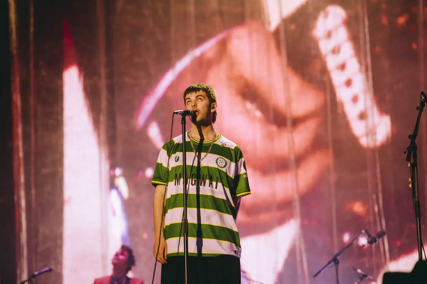Grian Chatten of Fontaines D.C. singing in the Cwmbran Celtic Mogwai shirt in front of the Reading Festival screens