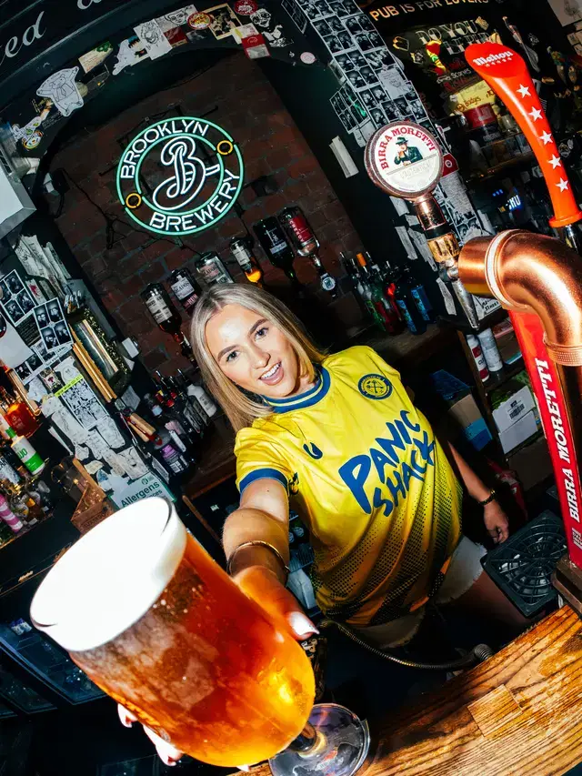 Model in the Panic Shack shirt holding out a pint